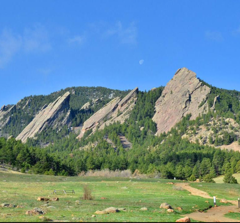 Scenic view of a mountain range called flatirons in Boulder with green trees and a clear blue sky.